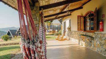 A covered outdoor area with a stone wall, wooden furniture, and a view of the mountains.
