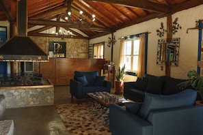 A cozy living room with a stone fireplace, blue sofas, and a wooden ceiling. - Pousada das Pedras (Camanducaia)