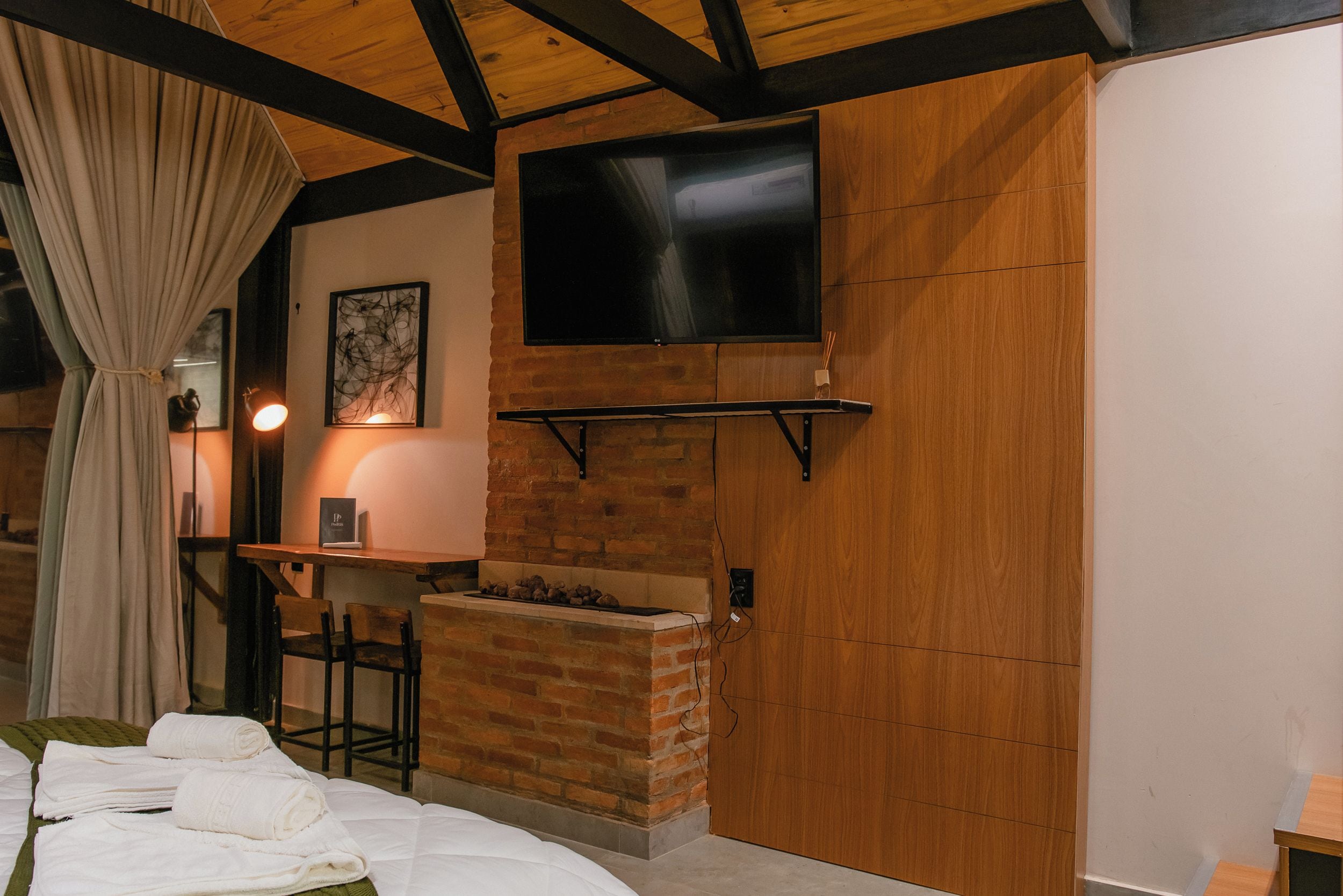 Quarto com lareira, TV de tela plana na parede, mesa com cadeiras e cama com roupa de cama branca.