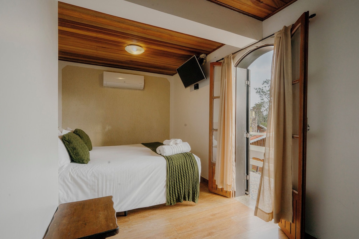A bedroom with a bed, a television, and a window with curtains.