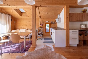 A modern interior with a wooden ceiling, a dining area with a table and chairs, a kitchen with white cabinets, and a view through a door. - Lumière du Plantin: 3 bedrooms with bathrooms, balconies, and mountain views (Les Allues)