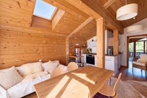 A wooden interior with a dining table, sofa, and kitchen area. - Lumière du Plantin: 3 bedrooms with bathrooms, balconies, and mountain views (Les Allues)