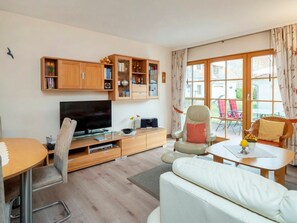A modern living room with a flat-screen TV, wooden cabinets, a sofa, and a dining area. - 4.1/t4 Holiday Home Park \"freesenbruch\" (Zingst)
