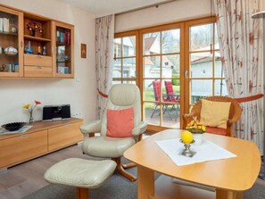 A room with a dining table, a cushioned chair, a bookshelf, and a view through a glass door. - 4.1/t4 Holiday Home Park \"freesenbruch\" (Zingst)