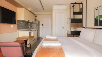 A hotel room with a bed, a small table, a chair, a TV, a kitchenette, and a bathroom.