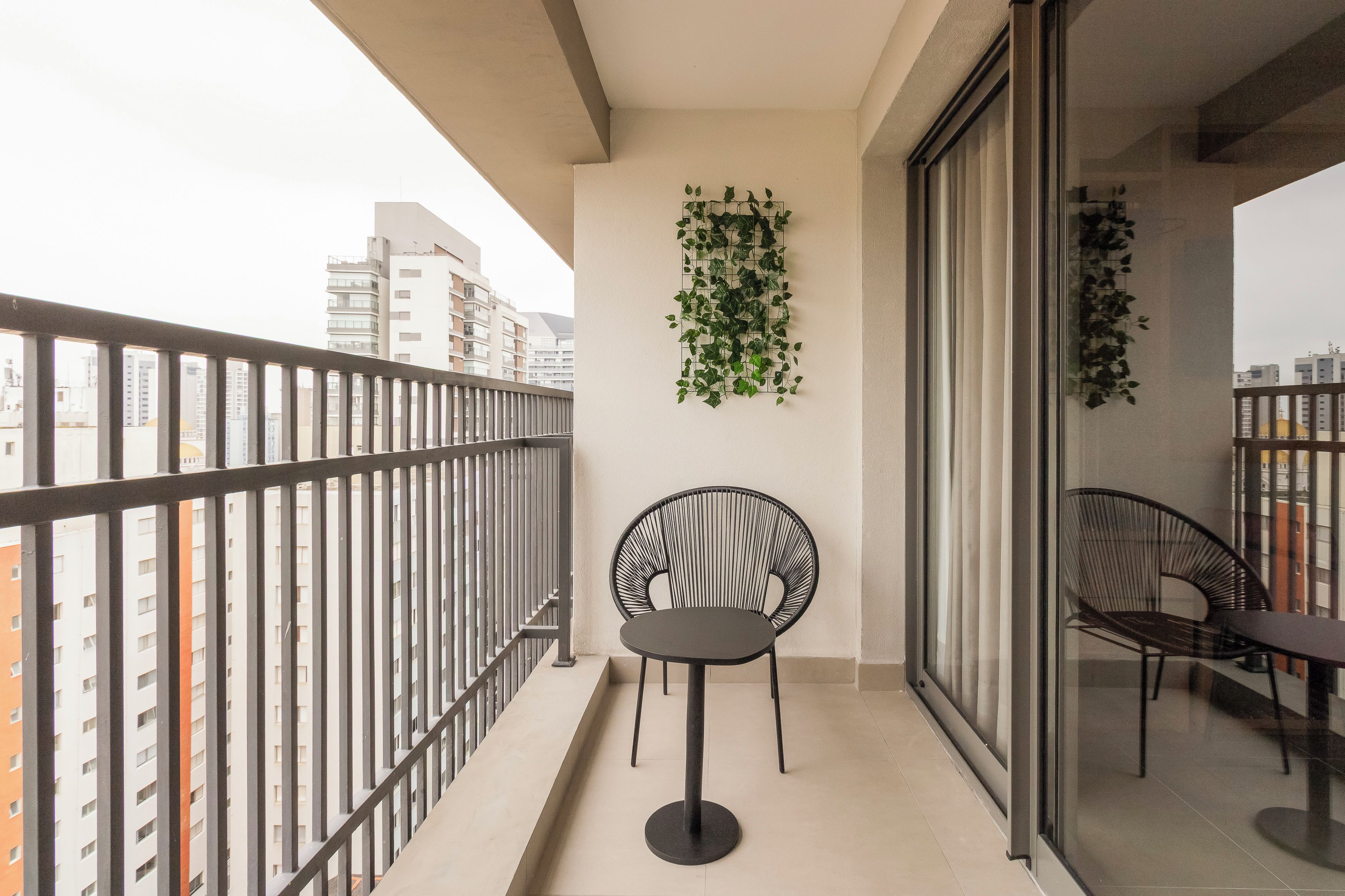 A balcony with a metal railing, a round black chair, a table, and a wall-mounted plant.