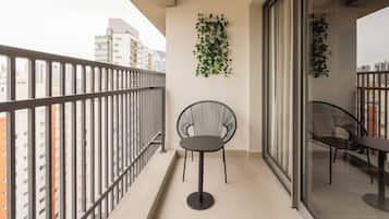 Uma varanda com guarda-corrimão de metal, uma cadeira preta arredondada, uma mesa e uma planta fixada na parede.