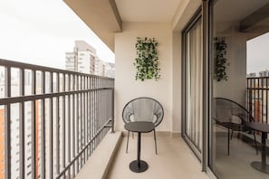 Uma varanda com guarda-corrimão de metal, uma cadeira preta arredondada, uma mesa e uma planta fixada na parede.