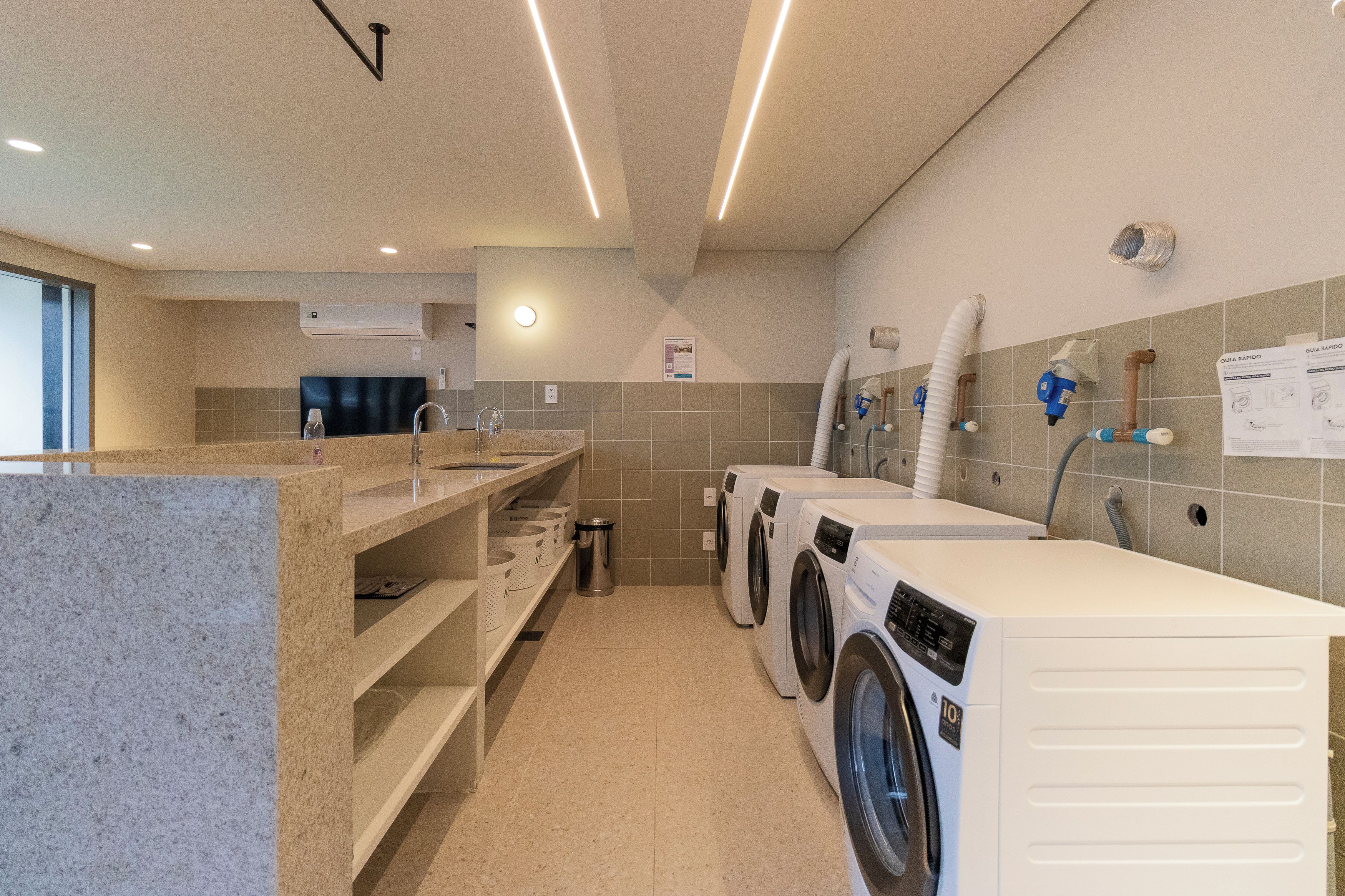 A modern laundry facility with multiple washing machines, a sink, and a trash bin.