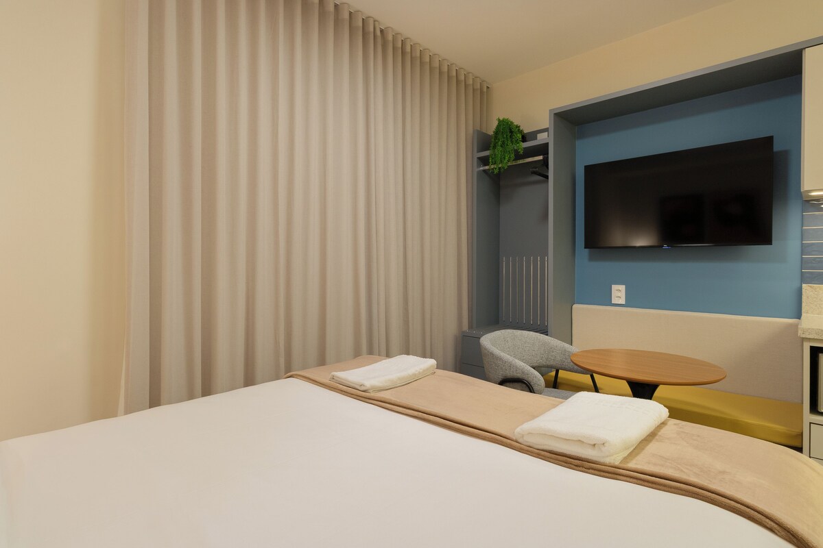A hotel room with a bed, a TV mounted on the wall, a small table, and a chair.