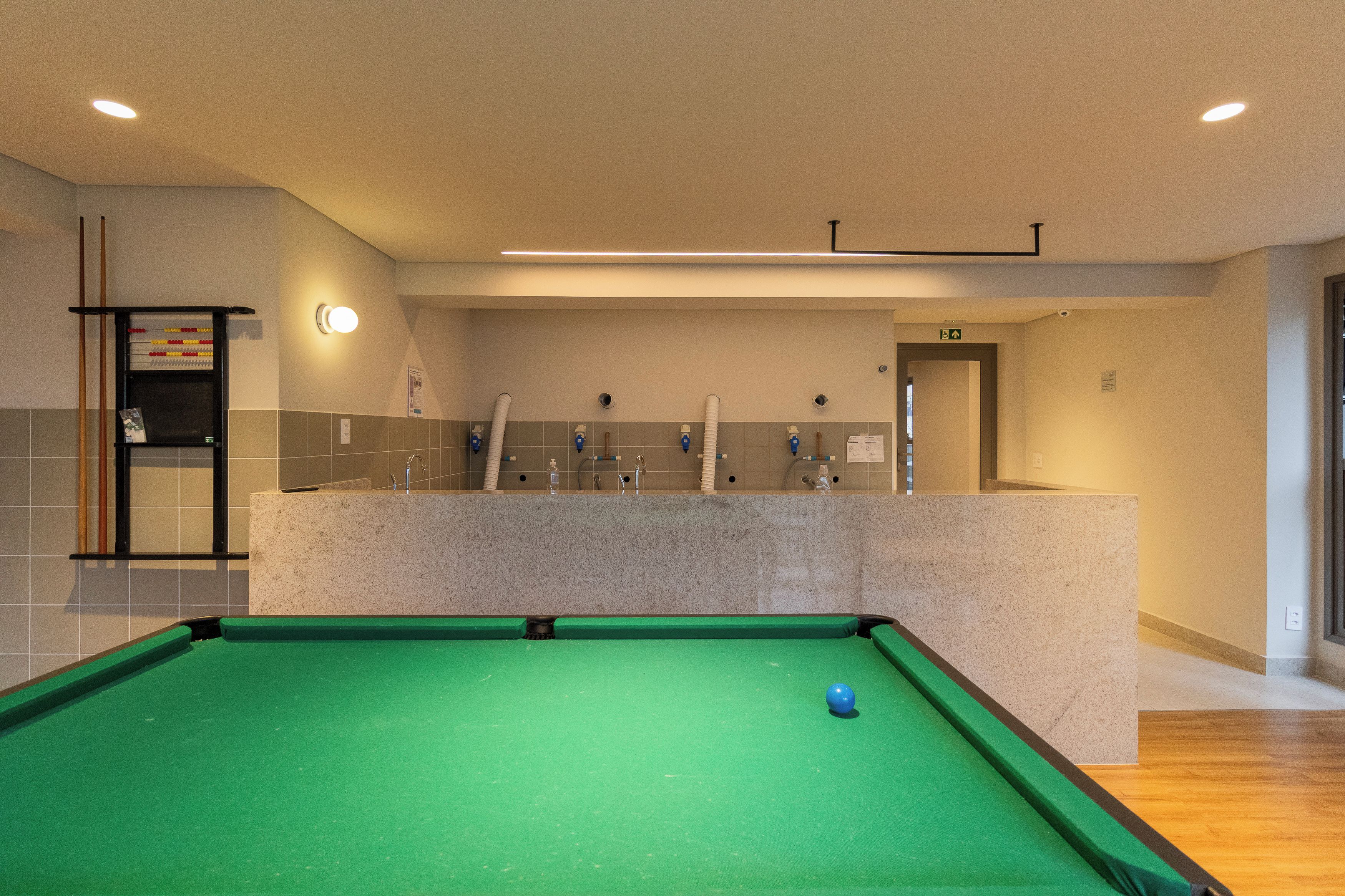 A pool table with a green felt surface and a blue cue ball, located in a room with a neutral color scheme and recessed lighting.