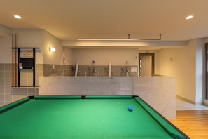 Mesa de bilhar com superfície de feltro verde e bola de cue azul, situada em ambiente com cores neutras e iluminação embutida.