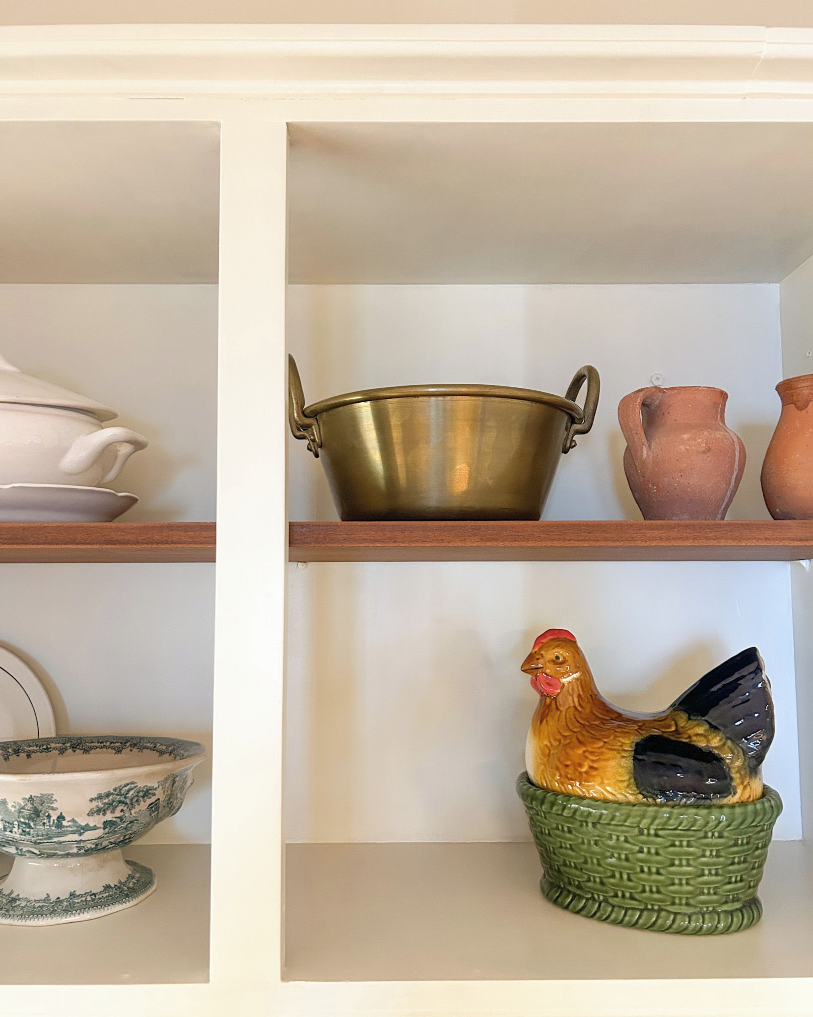 A shelf with various kitchenware including a metal pot, clay pots, and a ceramic chicken.