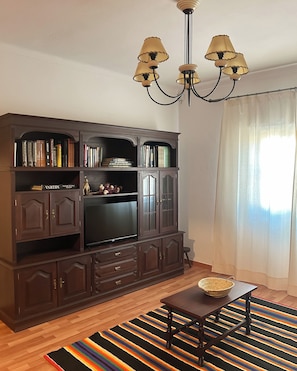 A living room with a dark wooden entertainment center, a flat-screen TV, a chandelier, and a colorful striped rug.