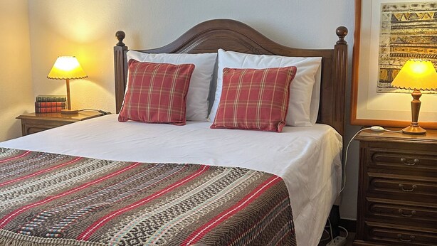 A neatly made bed with a patterned blanket, two bedside lamps, and a framed picture on the wall. - Vrbo Property (Benavila)