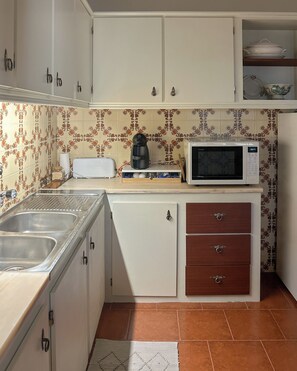 Cocina compacta con lavamanos, tostadora, cafetera, microondas y un refrigerador pequeño.