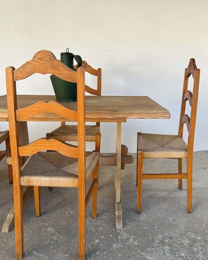 Une table à manger en bois avec des chaises, un arrosoir vert et un sol en béton.