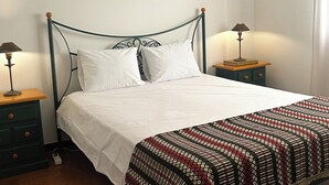 A bed with white bedding, a patterned blanket, and two bedside tables with lamps. - Vrbo Property (Benavila)