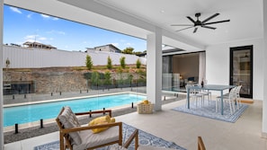 A modern outdoor pool area with a glass enclosure, a dining area with a table and chairs, and a ceiling fan. - Jewel of Carrickalinga - 14 Dorset Court (Carrickalinga)