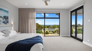 A bedroom with a large bed, a sliding glass door to a balcony, and a painting on the wall. - Jewel of Carrickalinga - 14 Dorset Court (Carrickalinga)