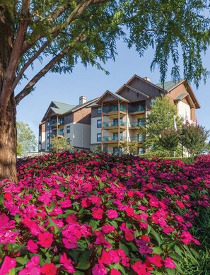 A multi-story hotel with balconies and a landscaped garden with pink flowers. - Sevierville | Pool & Mountains | 2BR Condo (Sevierville)