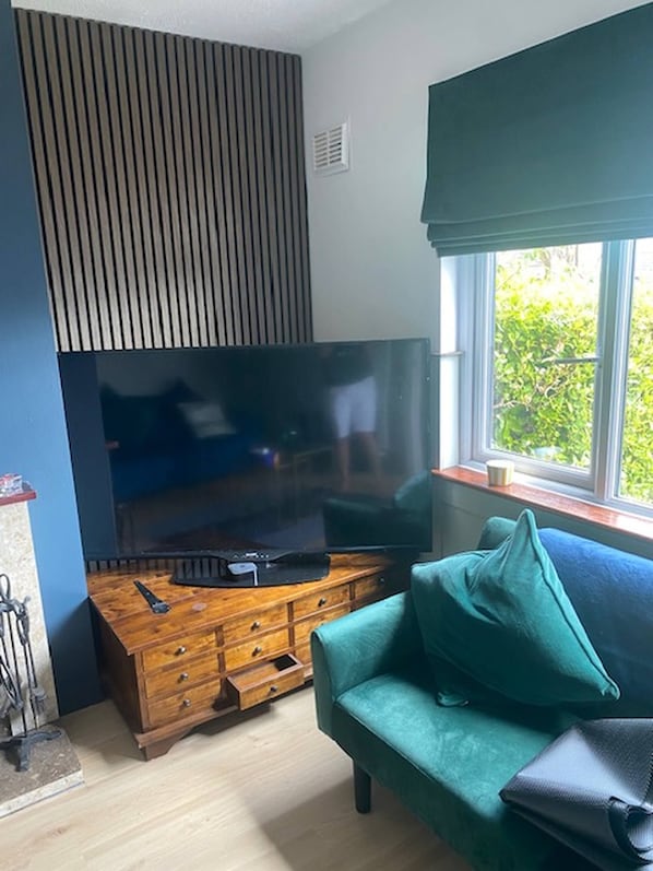 Una sala de estar con un televisor de pantalla plana sobre un soporte de madera, un sofá color turquesa y un ventanal con vistas a la vegetación.