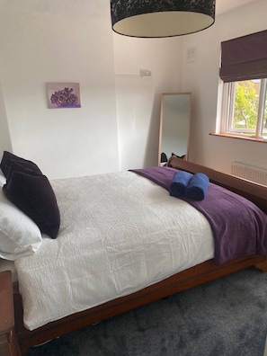 Un dormitorio con cama, mesita de noche, espejo, ventana con vistas y un cuadro colgado en la pared.