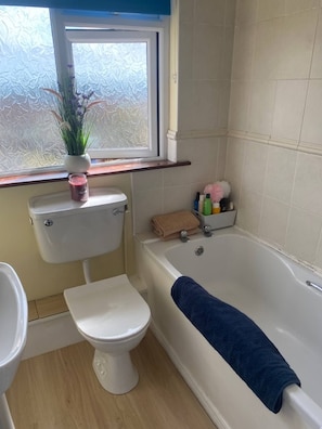 Un baño con inodoro, bañera y ventana con vidrio esmerilado.