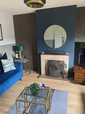 Una sala de estar moderna con un sofá azul, un espejo redondo, una chimenea y una mesa de centro de cristal.