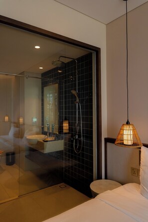 Un baño moderno con cabina de ducha de vidrio, lavamanos a la vista y una lámpara colgante.