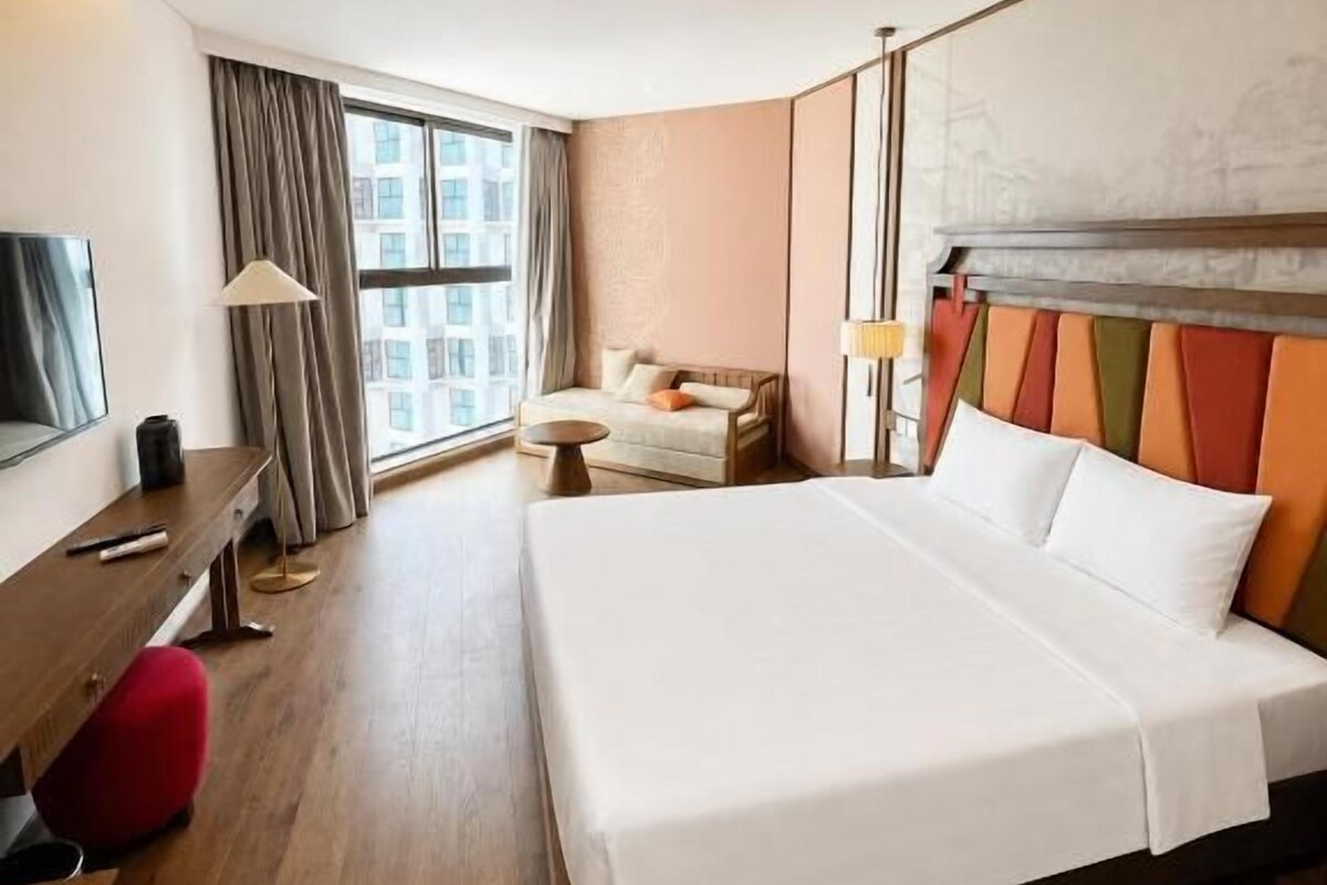 Habitación de hotel con cama, escritorio, silla, lámpara y ventana.