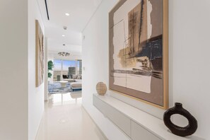 A modern interior with a hallway leading to a living area, featuring a large abstract painting, a vase, and a minimalist design. - Iconic 3 Bedroom with Panoramic View in Grand Bleu (Emaar Beachfront)