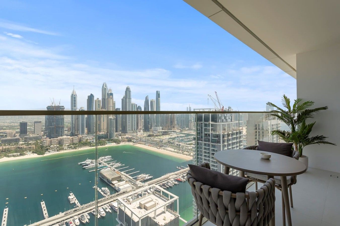 A balcony with a view of a city skyline, a marina, and a palm tree.