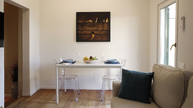 Un comedor con una mesa preparada para dos personas, sillas transparentes, un frutero y una copa de vino.