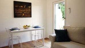 Un comedor con mesa blanca, sillas transparentes y un cuadro con marco negro en la pared.