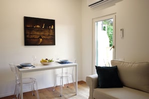 Uma área de jantar com mesa branca, cadeiras transparentes e uma moldura preta emoldurando uma imagem na parede.
