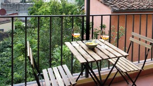 Un balcón con mesa y sillas de madera, un cuenco y dos copas de vino.