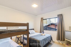 Ein Zimmer mit Etagenbetten, einem kleinen Tisch, einem Fenster mit Vorhängen und Blick auf Gebäude.