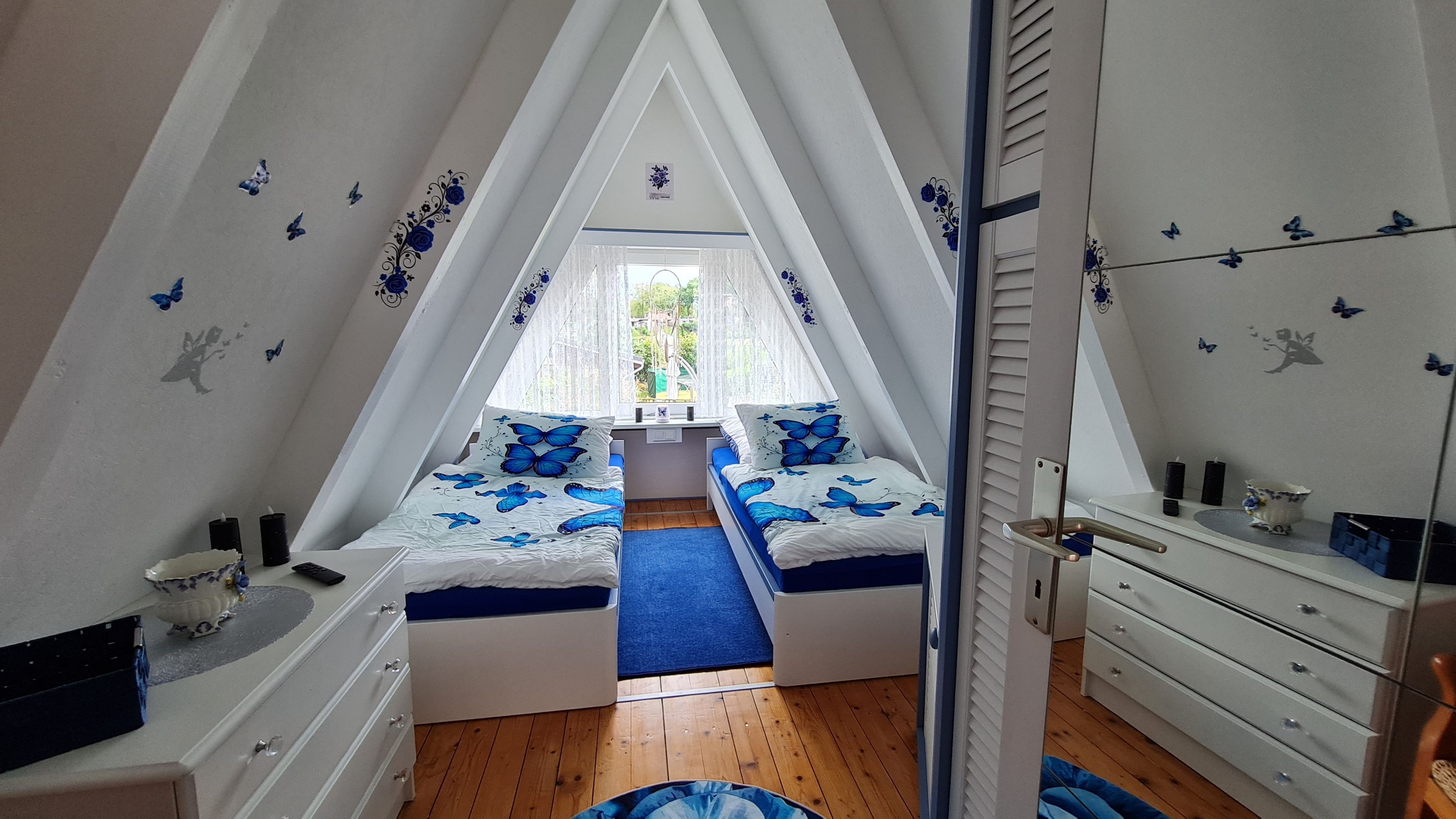 A triangular attic bedroom with two beds, a dresser, and a mirror.