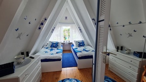Quarto sótão triangular com duas camas, uma cômoda e um espelho.