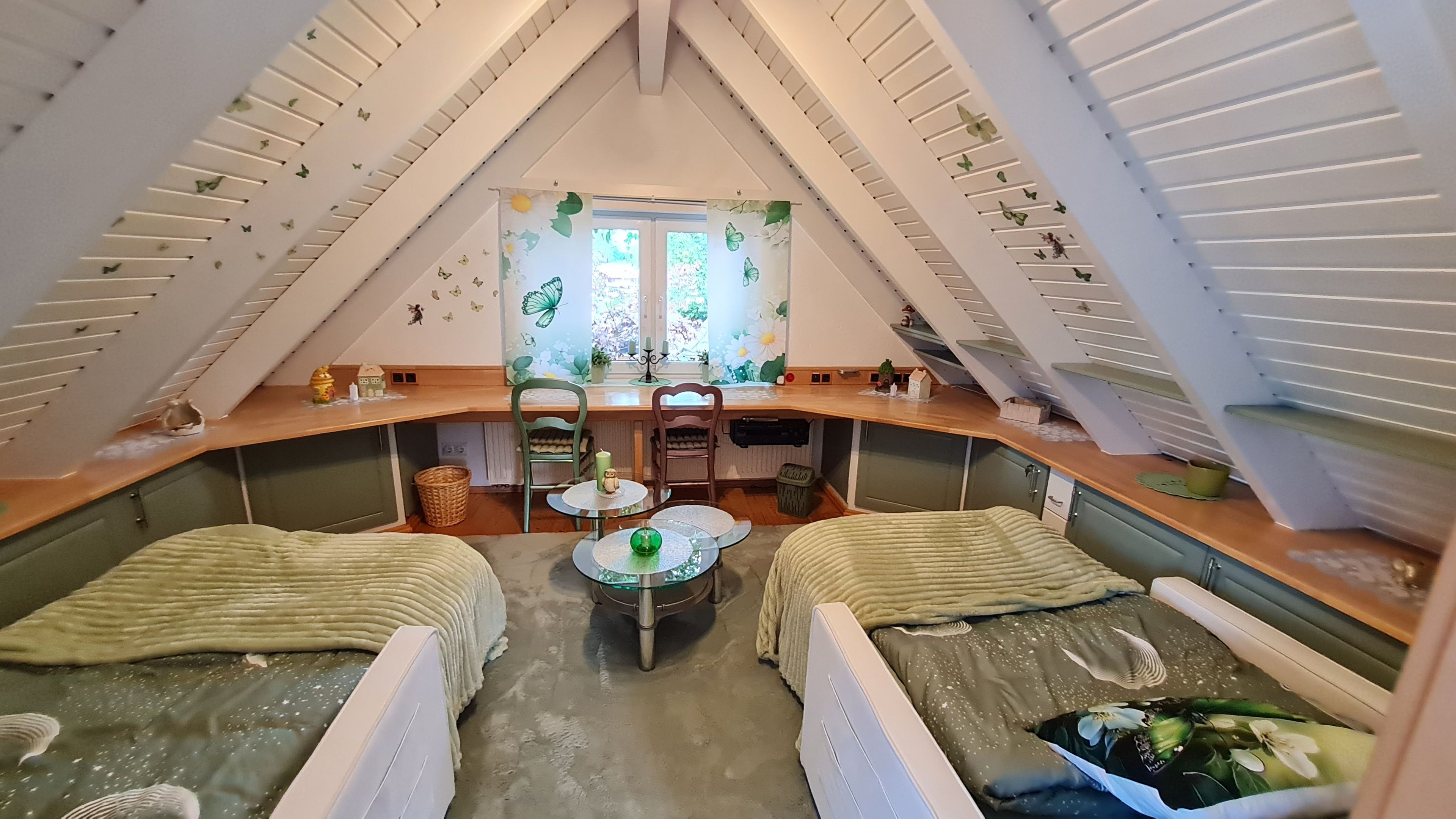 Un dormitorio acogedor en el ático con dos camas, una mesita pequeña y un ventanal con cortinas florales.