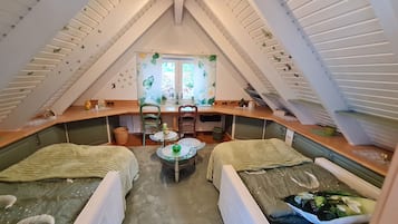 Un dormitorio acogedor en el ático con dos camas, una mesita pequeña y un ventanal con cortinas florales.