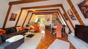 Una sala de estar acogedora con un sofá, una mesa de centro y sillones naranjas. Se ve un comedor con una mesa y sillas al fondo.