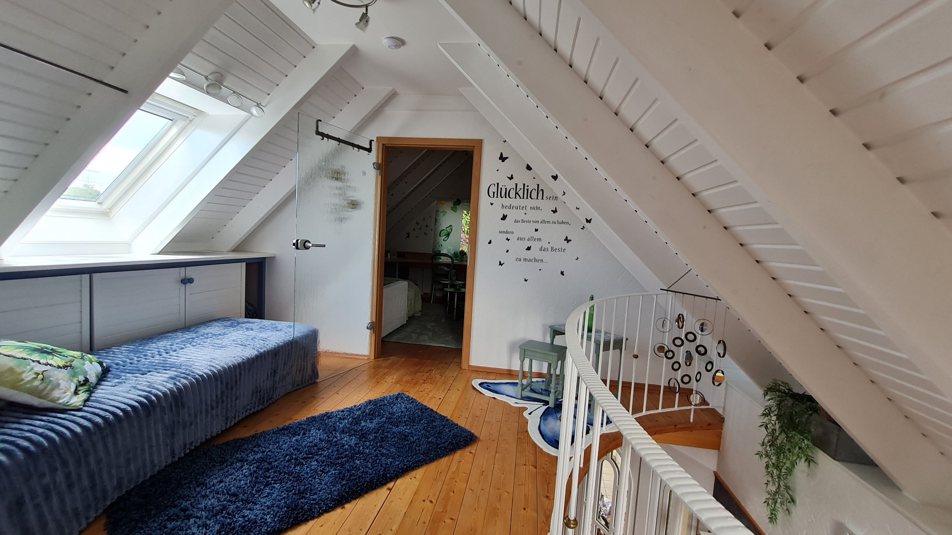 Ein Zimmer mit schrägen Wänden, einem Bett, einem Schreibtisch und einer Treppe.