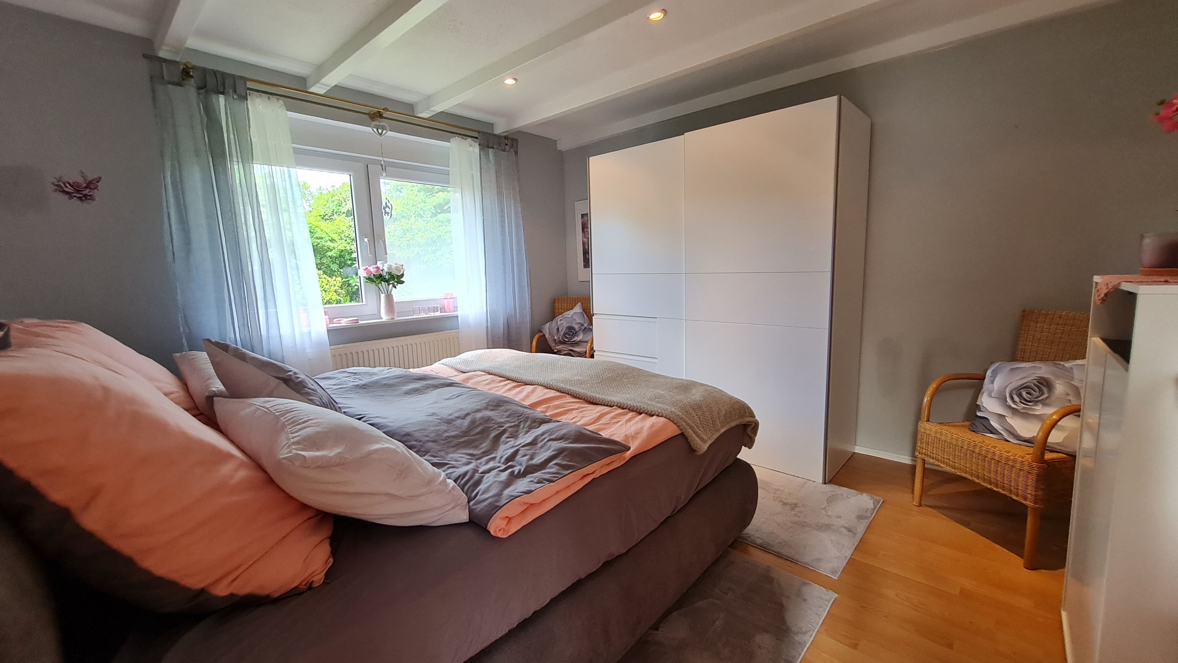 Ein Schlafzimmer mit Bett, Stuhl, Kleiderschrank und einem Fenster mit Vorhängen.