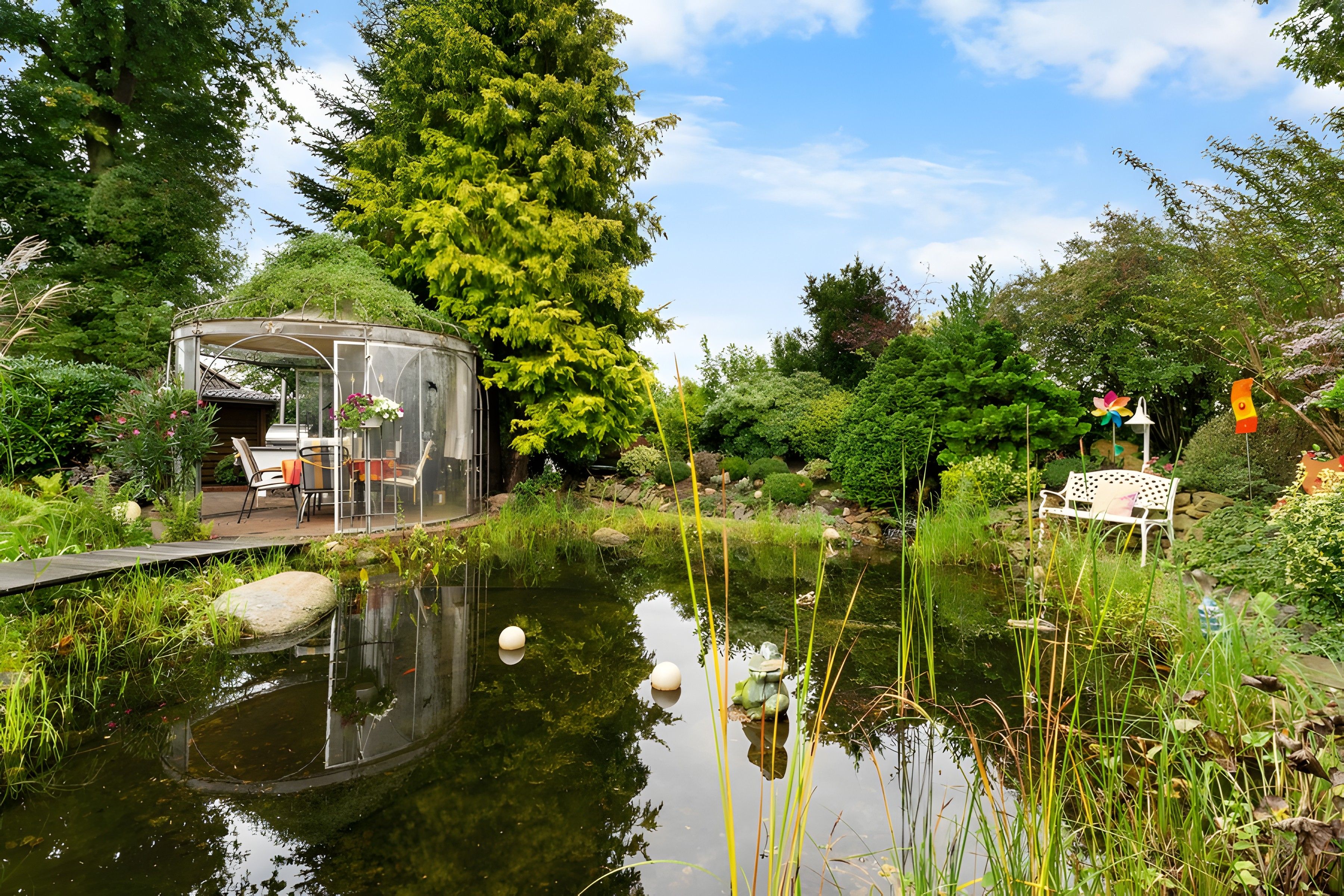 Ein Garten mit Teich, Laube und Bank.