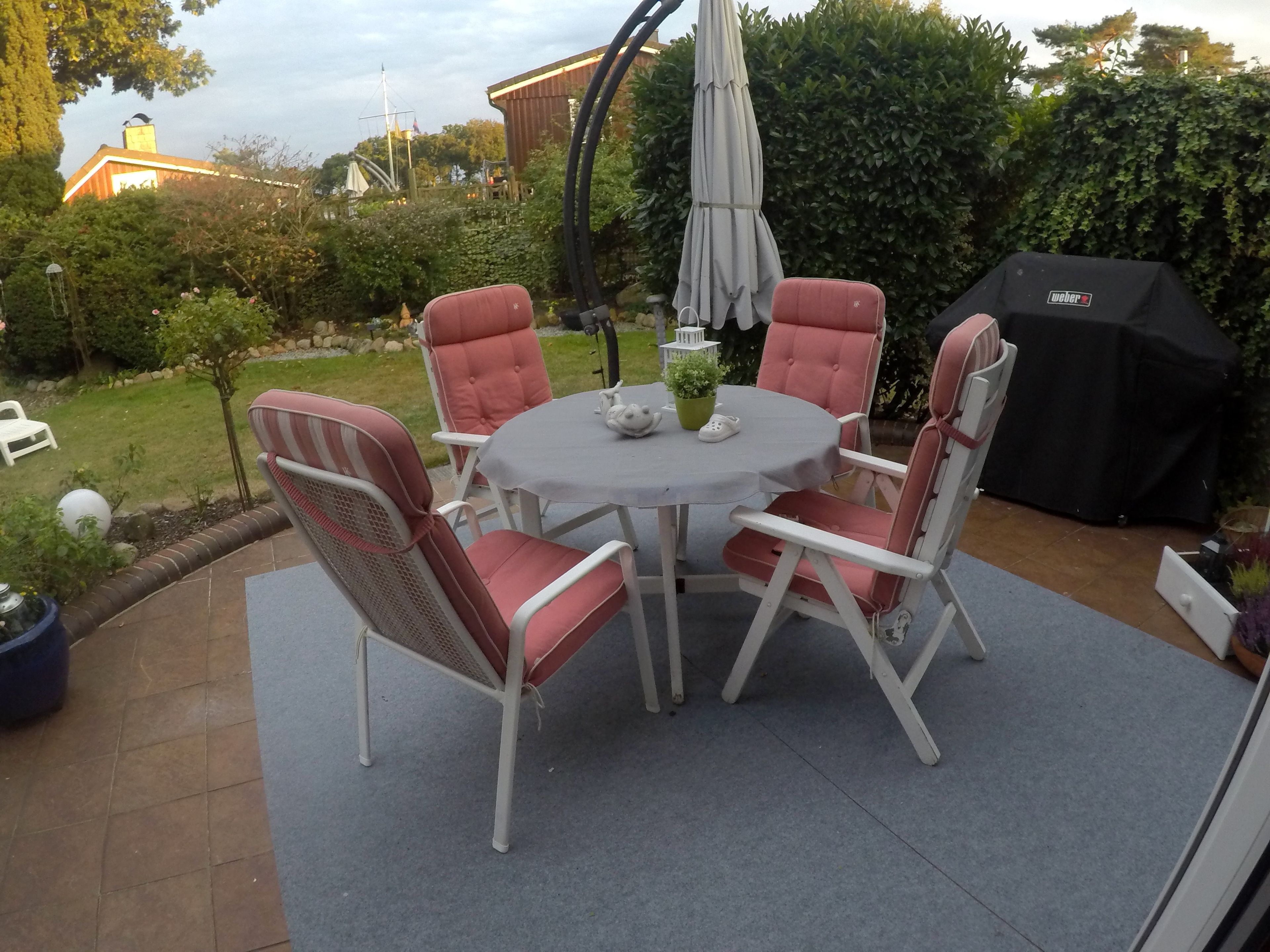 Eine Terrassengruppe im Freien mit rundem Tisch und vier Stühlen, umgeben von einem Garten.