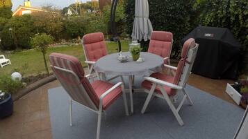 Eine Terrassengruppe im Freien mit rundem Tisch und vier Stühlen, umgeben von einem Garten.