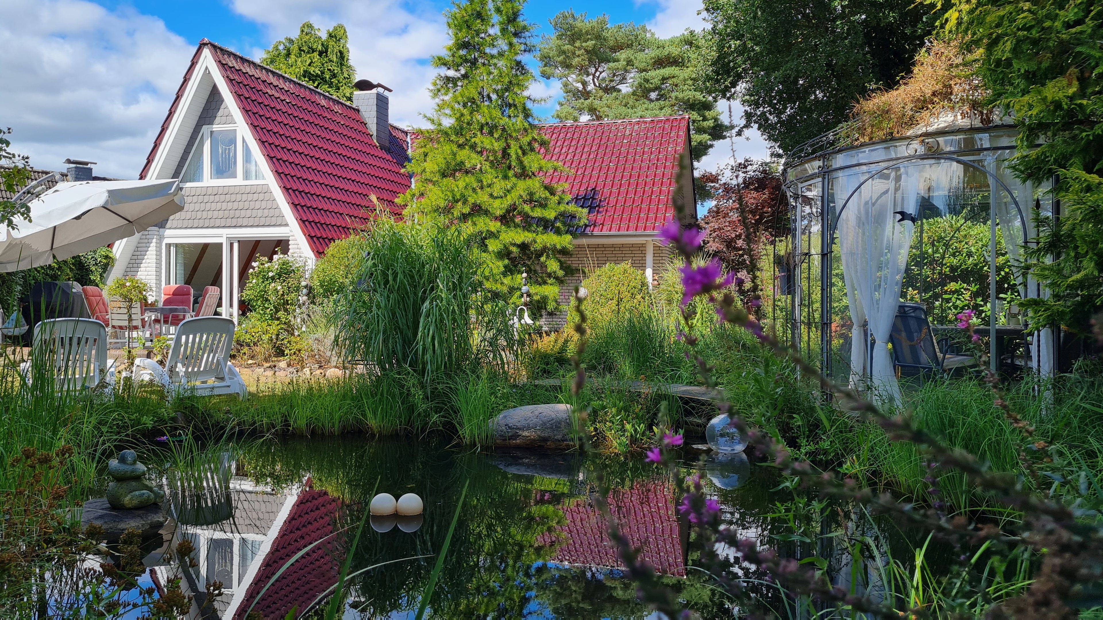 A house with a red roof, a pond with a statue, and outdoor furniture.