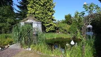 Ein Garten mit Teich, Laube und verschiedenen Pflanzen.